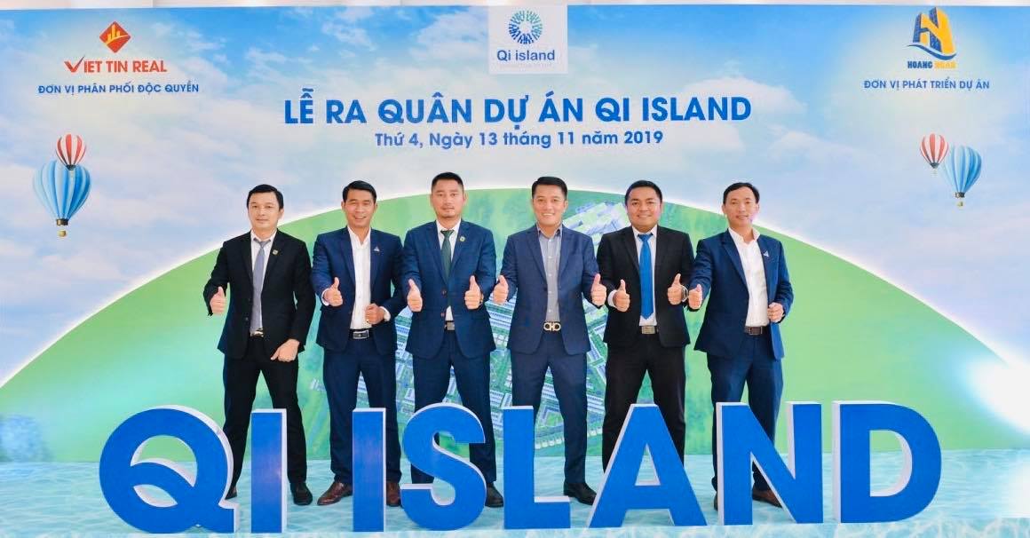 ^ người đàn ông mặc vest giơ tay ra phía trước và chữ Qi Island màu xanh