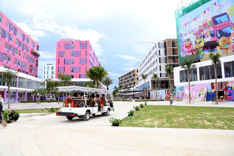 Bên trong dự án Cocobay, xe điện chở khách, sân cỏ, xung quanh là các tòa nhà màu hồng, trắng.