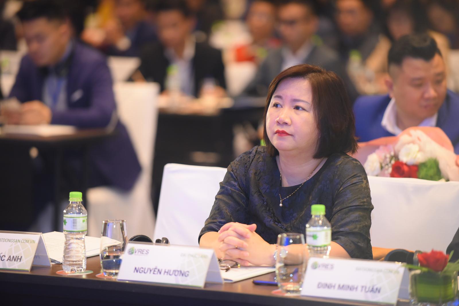 Chân dung một phụ nữ trung tuổi tóc ngắn, mặc váy đen đang ngồi nghe chăm chú.