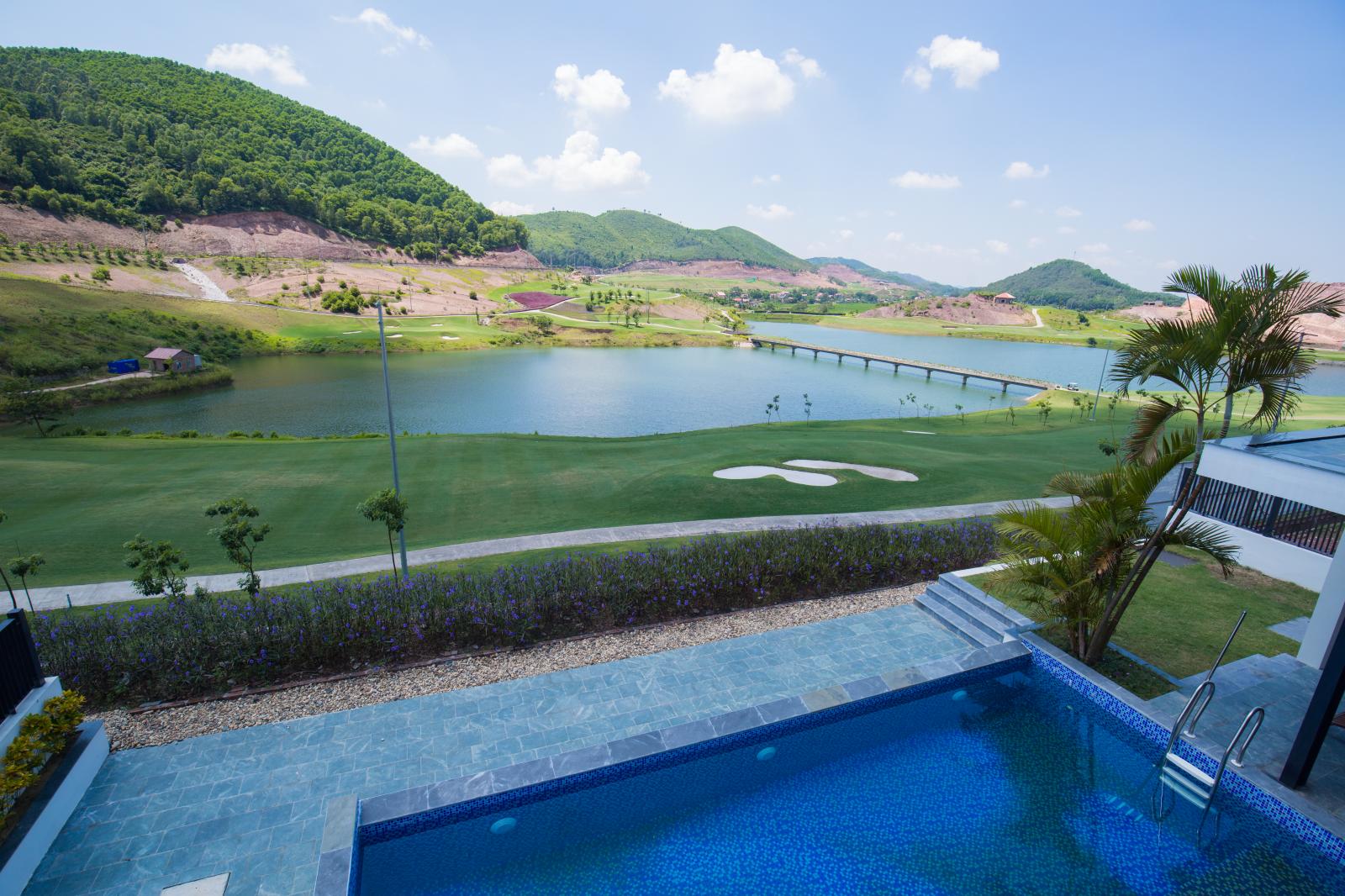 hình ảnh sân golf nhìn từ bể bơi khu biệt thự, phía trước có dòng sông và đồi núi