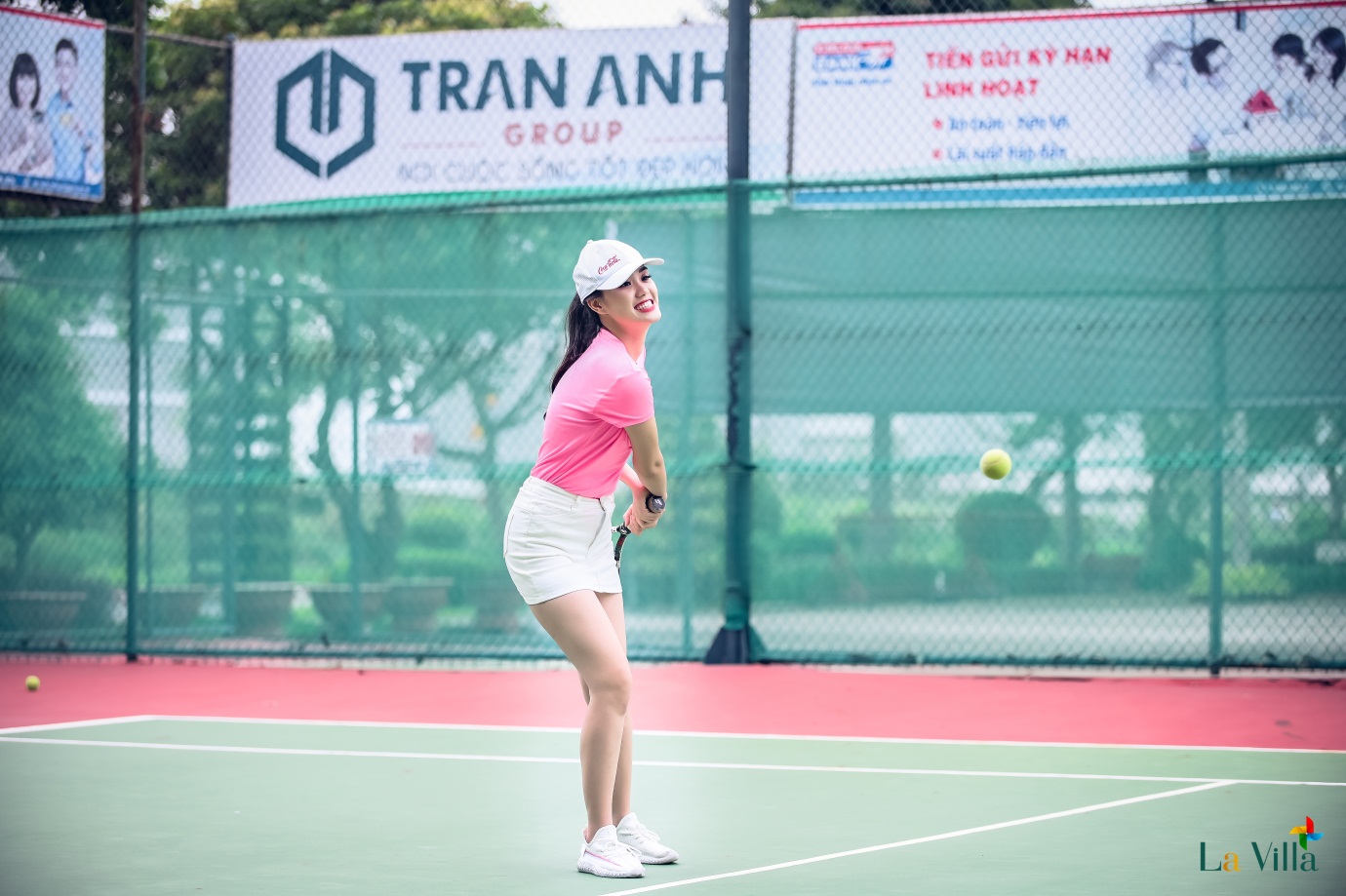 1 cô gái mặc áo hồng, chân váy trắng đang chơi tennis