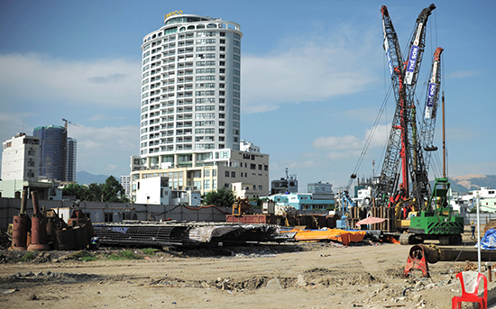 Khu đất trống ngổn ngang vật liệu, cẩu tháp, bên ngoài là những tòa nhà cao tầng.