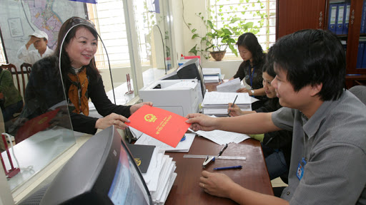 hình ảnh trong văn phòng đăng ký đất đai, 2 người đang trao và nhận cuốn sổ đỏ